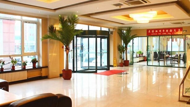 Un hall d’hôtel avec une entrée en verre, des plantes en pot et un tapis rouge menant à un escalier.