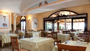 Un restaurant doté de nombreuses tables et chaises, d’un plafond haut orné d’éléments décoratifs et de grandes fenêtres laissant entrer la lumière naturelle.