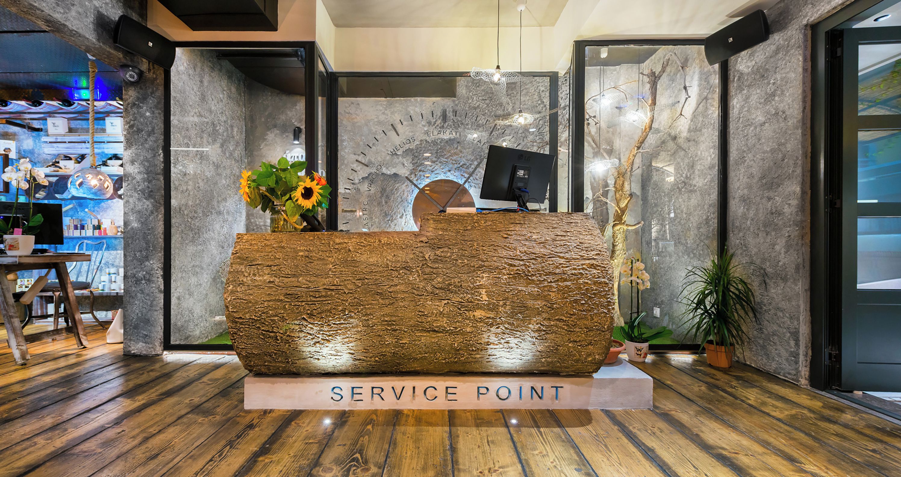 Un comptoir d’accueil portant l’inscription « POINT D’INFORMATION », avec une texture en bois rustique, un vase rempli de fleurs et un luminaire moderne.