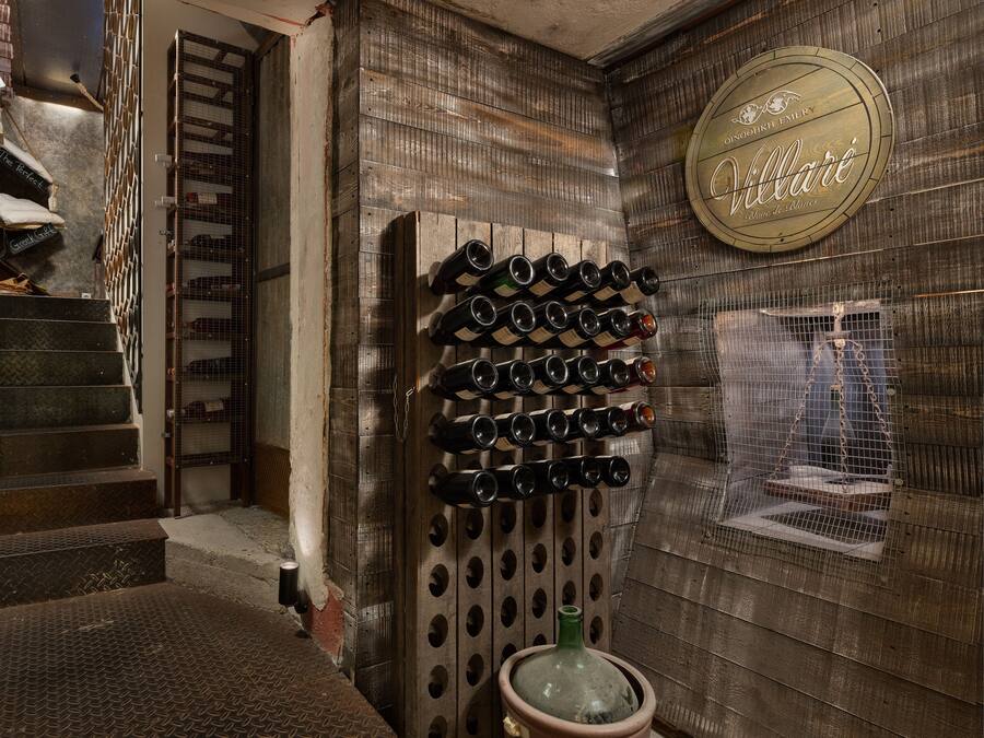 Een wijnkelder met een houten wand, een wijnrek en een wenteltrap.