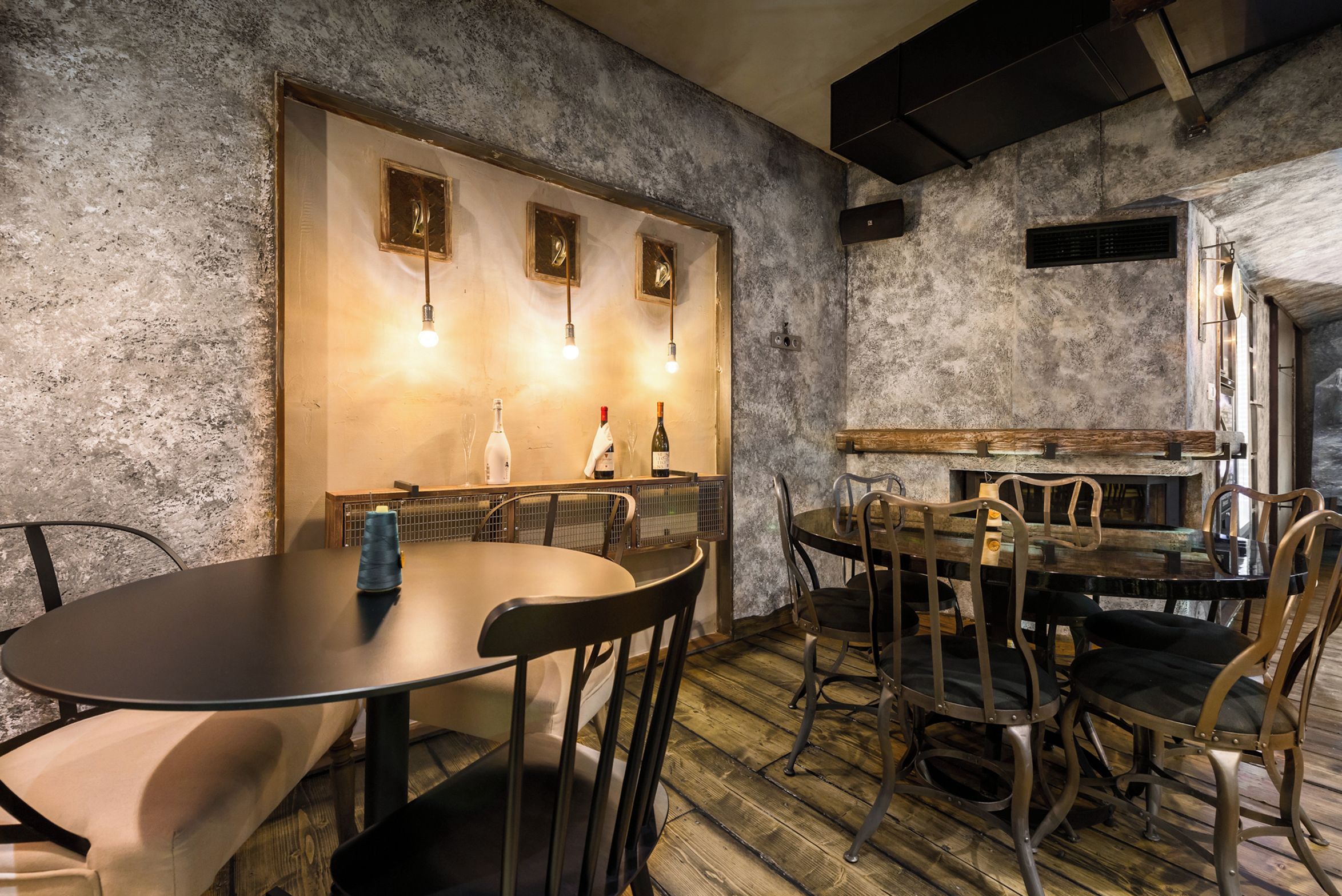 A rustic interior with a round table, chairs, and a bar area.