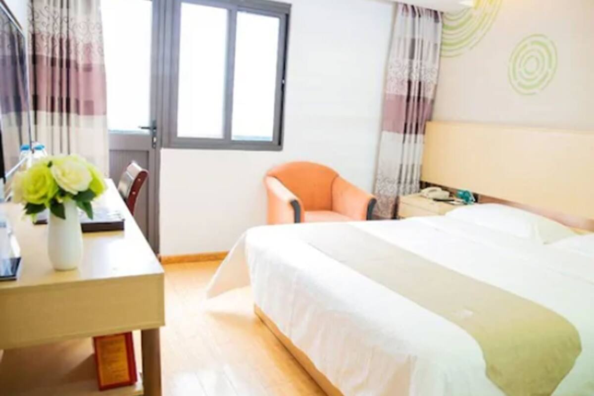 Een hotelkamer met een bed, een bureau met een bloevas, een stoel en een raam met gordijnen.