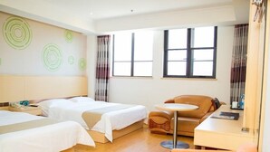 Habitación de hotel con dos camas, un sofá, una mesita y una ventana con cortinas.