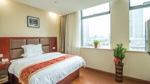 A hotel room with a large bed, a nightstand, a telephone, a window with a city view, and a potted plant. - Greentree Inn Suzhou Dongwu North Road Business Hotel (Suzhou)