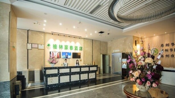A hotel reception area with a marble floor, a reception desk, a wall-mounted TV, and a floral arrangement on a table. - Greentree Inn Suzhou Dongwu North Road Business Hotel (Suzhou)