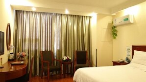 Una habitación de hotel con una cama, dos sillas, un escritorio con lámpara y una ventana con cortinas.