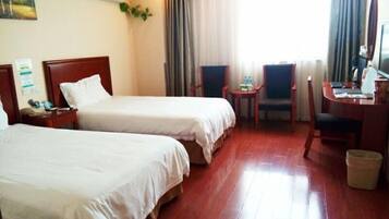 A hotel room with two beds, a desk with a chair, a small table with a chair, and a trash bin.