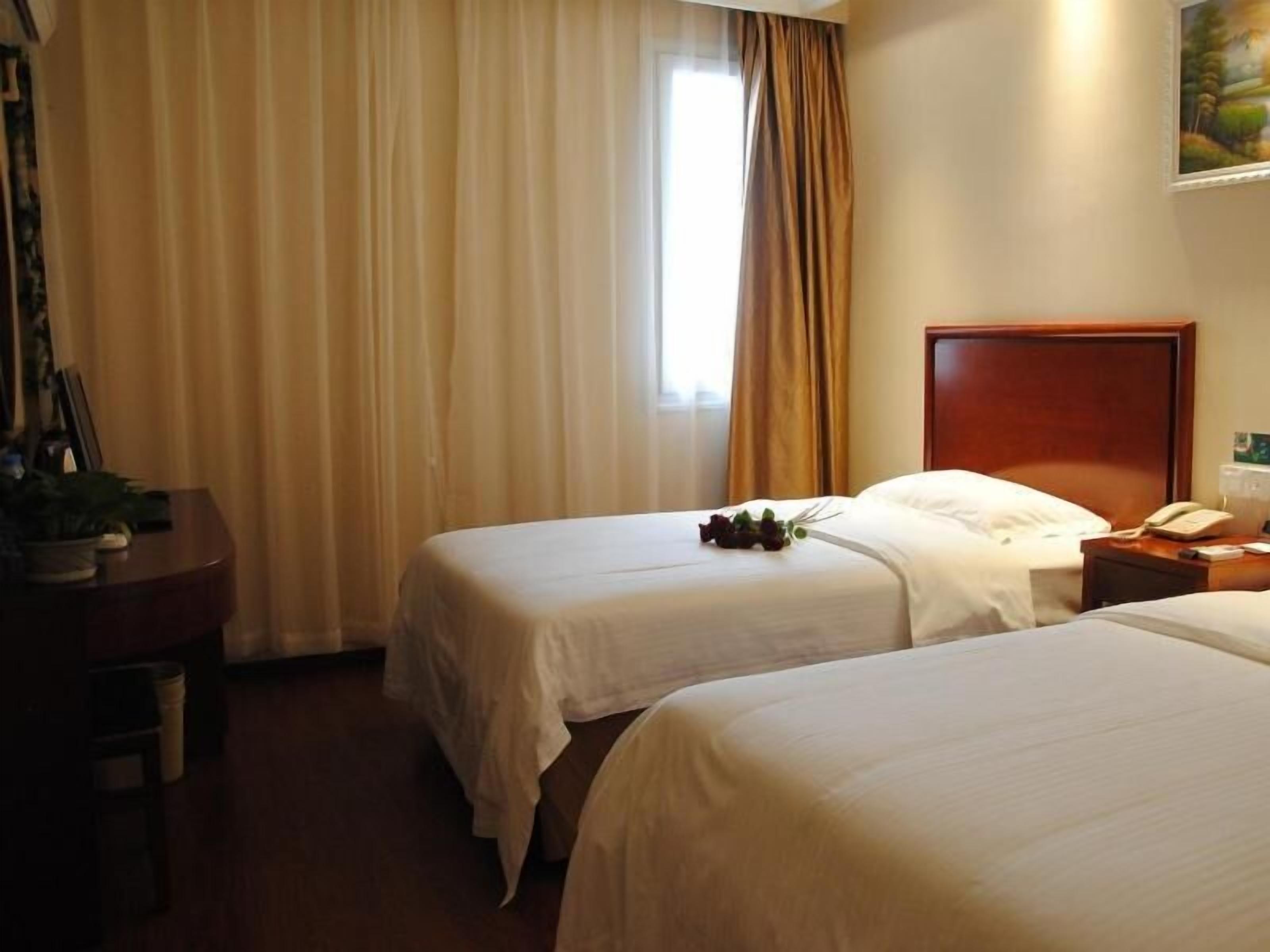 A hotel room with two single beds, a wooden headboard, a bedside table with a telephone, and a window with curtains.