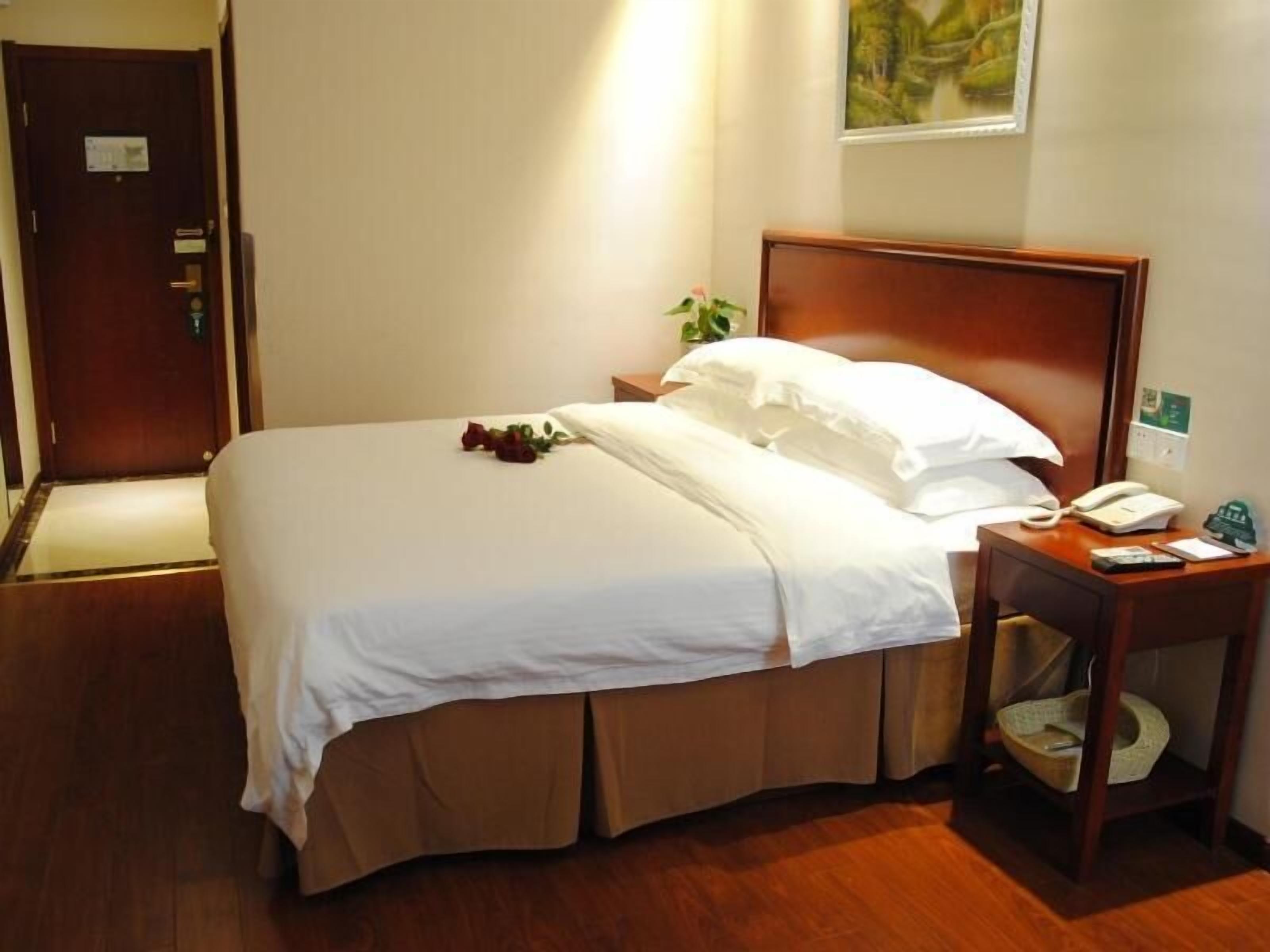 A hotel room with a wooden bed, white linens, a bedside table with a phone and a basket, and a door with a sign.