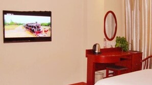 Una habitación de hotel con una cama, un escritorio con espejo, un televisor mostrando un tren y una planta.