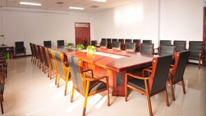 Un salón de conferencias con una larga mesa y sillas, una puerta y una pared blanca.