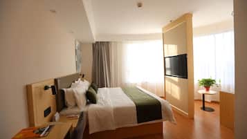 Habitación de hotel con cama, escritorio, televisor y planta en maceta.