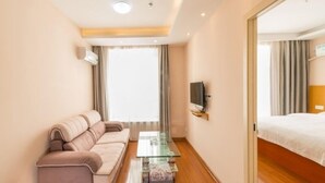 Une chambre d’hôtel avec un canapé, une table basse en verre, un téléviseur fixé au mur et un lit doté d’une tête de lit en bois.
