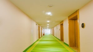 Un long couloir étroit, typique d’un hôtel, avec une moquette verte et des portes en bois de chaque côté.