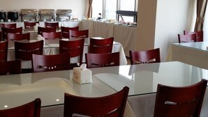 Une salle de conférence dotée de tables en verre et de chaises rouges, de grandes fenêtres et d’un espace buffet à l’arrière-plan.
