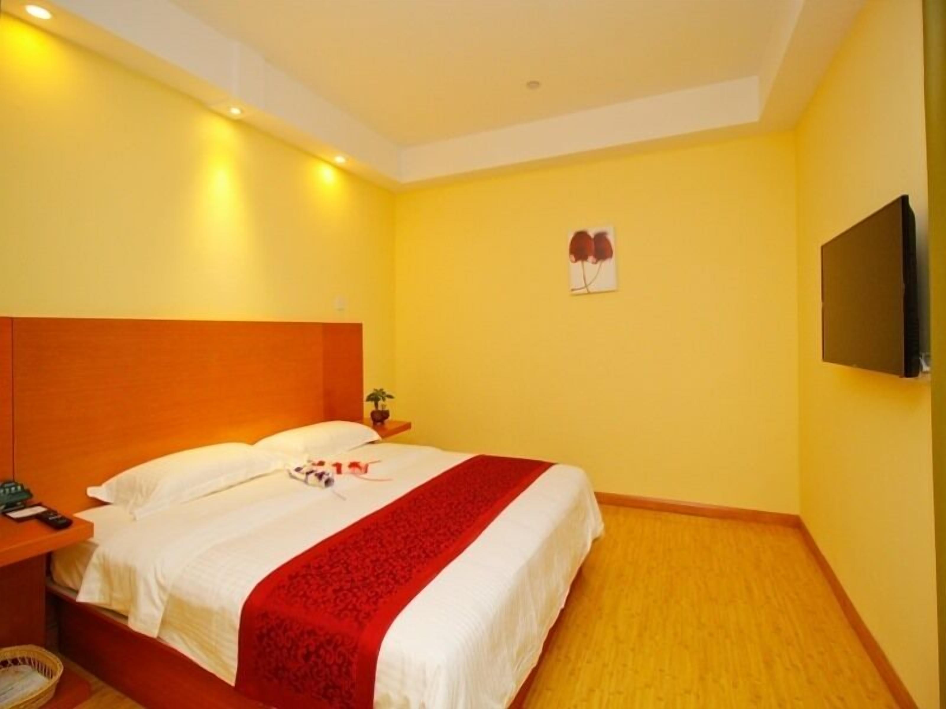 A hotel room with a bed, a nightstand, a TV mounted on the wall, and a small potted plant.