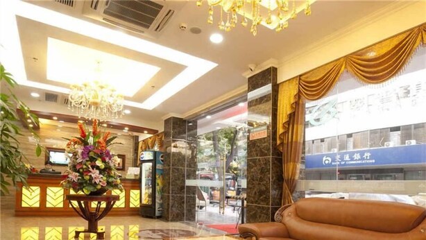 A hotel lobby with a reception desk, a large floral arrangement, a leather sofa, and a view of the street outside. - Greentree Inn Guangdong Shantou Changping Road Exp (Shantou)