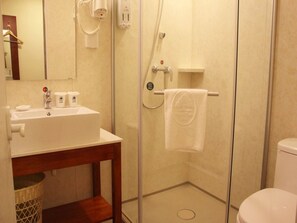 Ein Badezimmer mit Duschkabine aus Glas, einem Waschbecken mit Pflegeprodukten und einem Handtuch auf einem Wäscheständer.