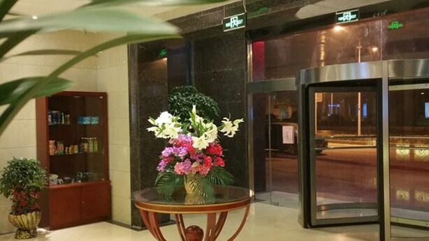 Un vestíbulo con una mesa de vidrio que sostiene un arreglo floral, una recepción y una puerta giratoria.