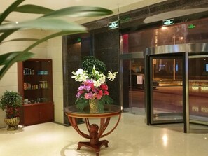 A lobby with a glass-top table holding a floral arrangement, a reception desk, and a revolving door. - GreenTree Inn JXuZhou East Third Ring Road XCMG Heavy Machinery Hotel (Xuzhou)