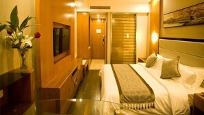 A hotel room with a bed, a TV, a desk, and a plant.