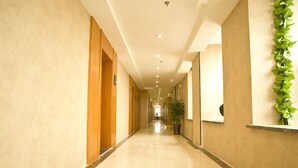 A long, well-lit hallway with a marble floor, wooden doors, and a potted plant on the right.