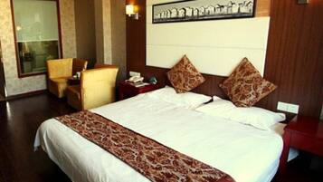 A hotel room with a large bed, a chair, a desk, and a wall-mounted picture.