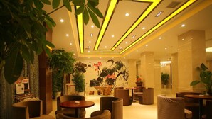 Un hall d’entrée spacieux, doté d’un mobilier moderne, comprenant des tables rondes et des fauteuils confortables, et bien éclairé grâce à des luminaires au plafond.