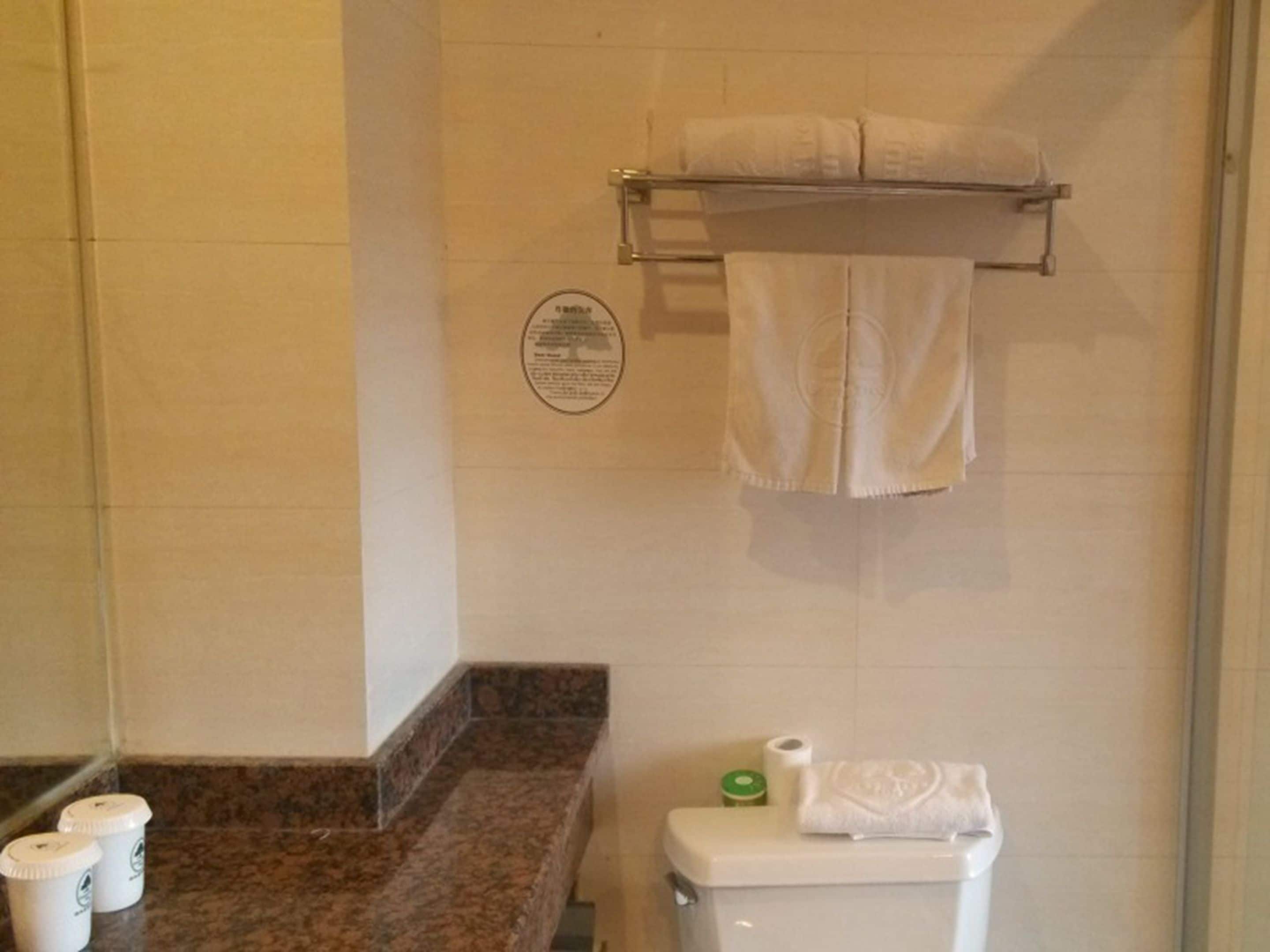 A bathroom with a toilet, a towel rack with a towel, and a trash bin.