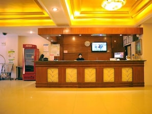 A hotel reception area with a wooden reception desk, a clock, a television, and a vending machine. - Greentree Inn Jiangsu Suzhou Xiangcheng Huolidao Isla (Suzhou)
