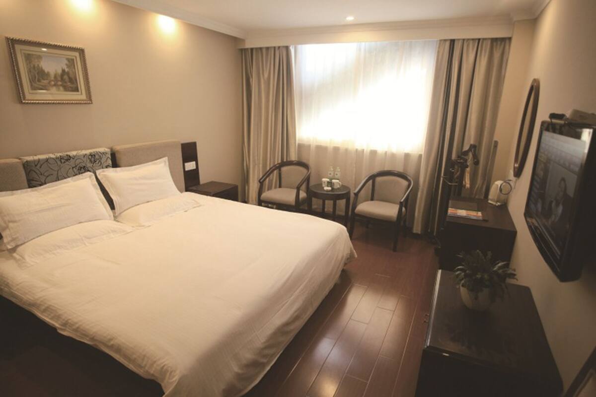 Ein Hotelzimmer mit einem großen Bett, zwei Stühlen, einem kleinen Tisch, einem Fernseher und einem Fenster mit Vorhängen.