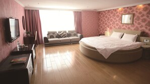 Ein Schlafzimmer mit einem runden Bett, einem Sofa, einem Fernseher und einem Schreibtisch.