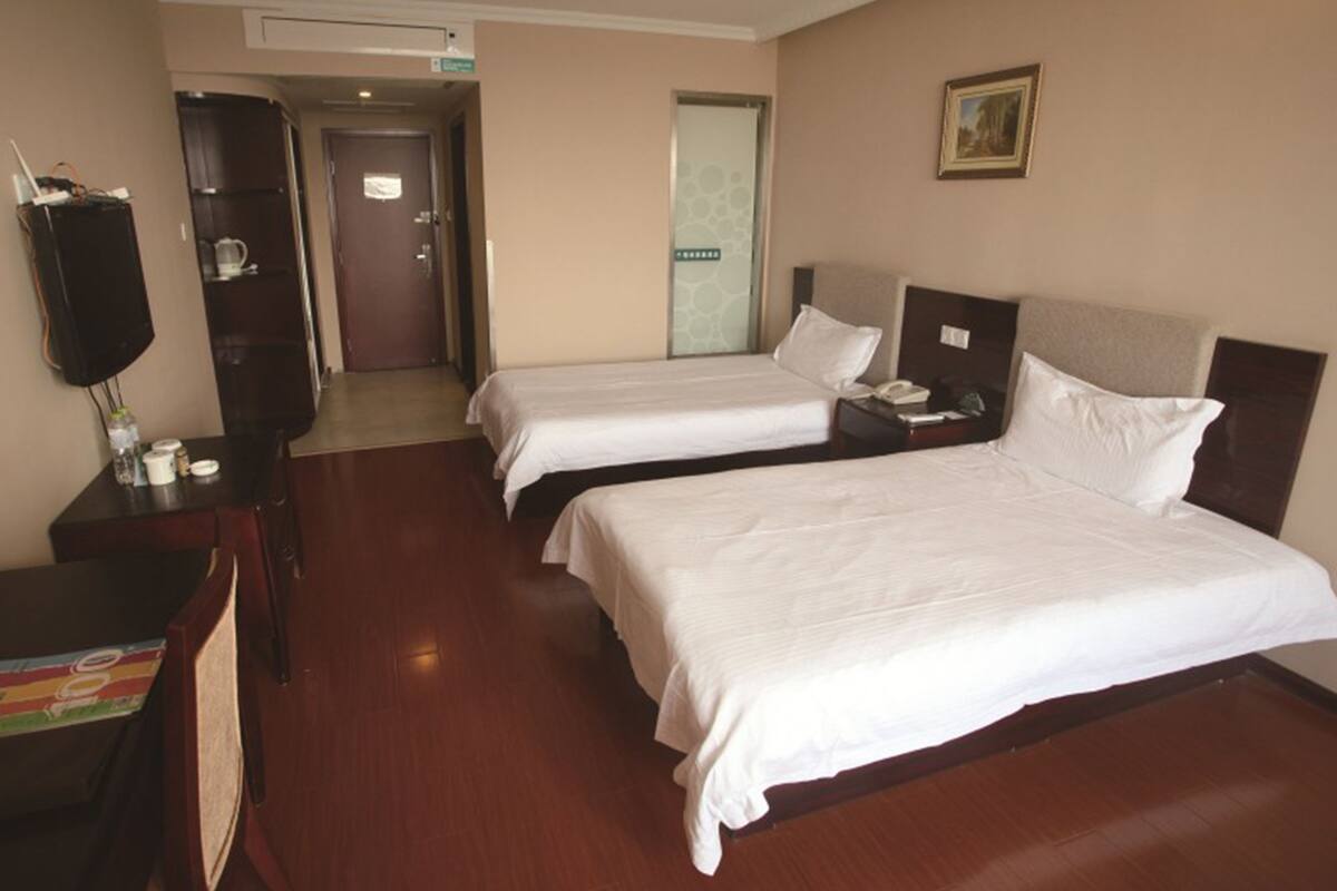 Ein Hotelzimmer mit zwei Betten, einem Schreibtisch, einem Fernseher und einer Tür zu einem Badezimmer.