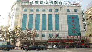 Ein Hotel mit einer großen Schrifttafel in chinesischen Schriftzeichen, zahlreichen Fenstern und einer Reihe geparkter Autos davor.