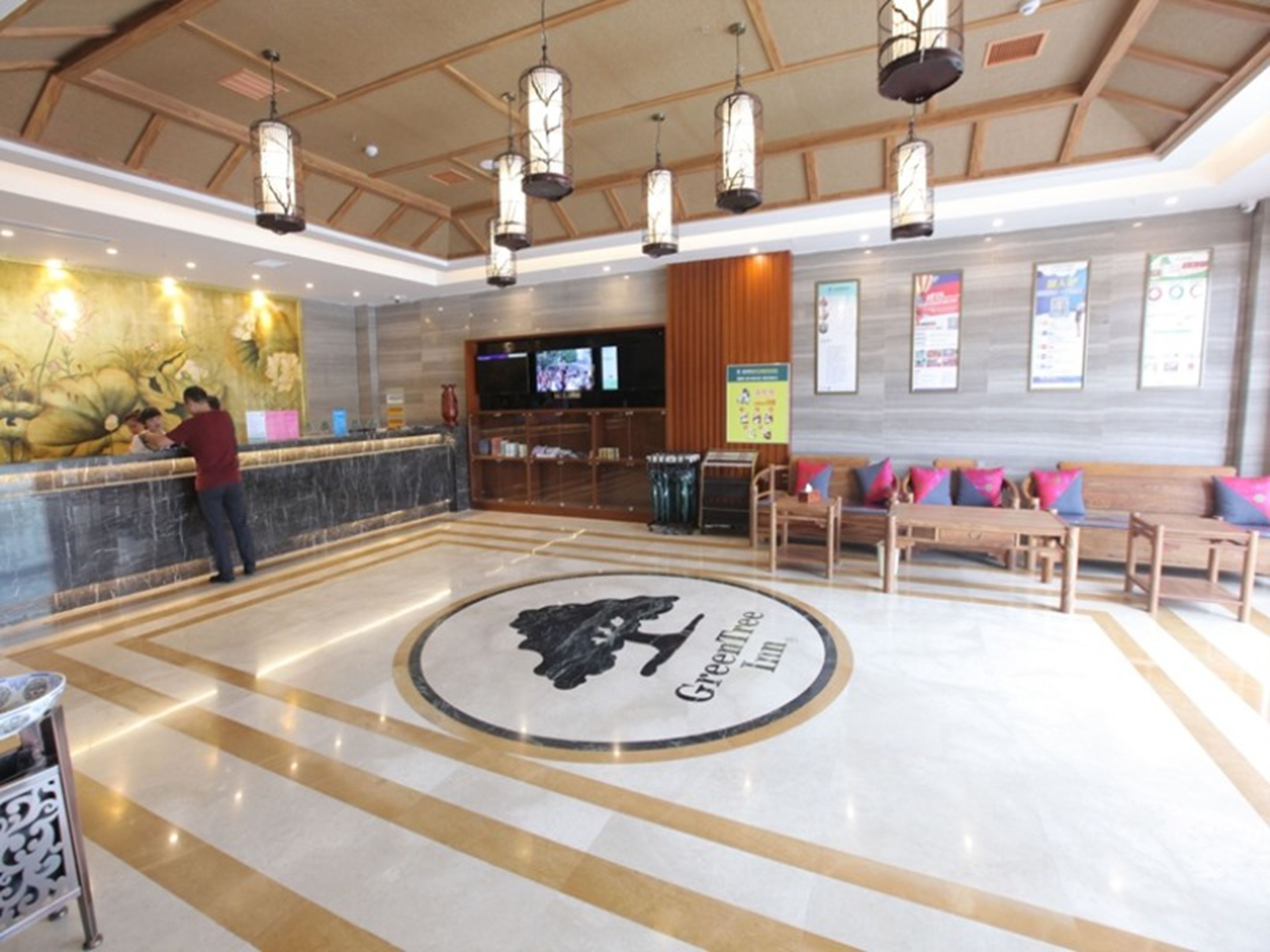 A lobby with a reception desk, a large circular logo, a television, and seating area with cushions.
