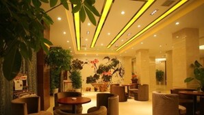 Un hall amplio con mobiliario moderno, que incluye mesas redondas y sillones acolchados, y está bien iluminado con luces de techo.