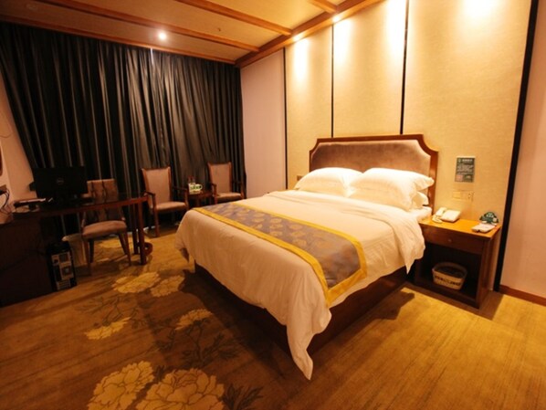 A hotel room with a large bed, a desk with a computer, two chairs, and a small trash bin.