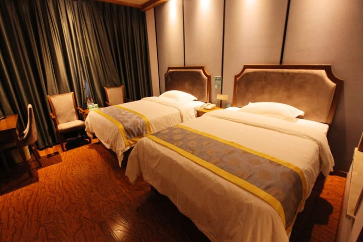 Ein Hotelzimmer mit zwei Betten, Holzboden, einem Stuhl, einem Schreibtisch und einem Nachttisch mit Lampe.