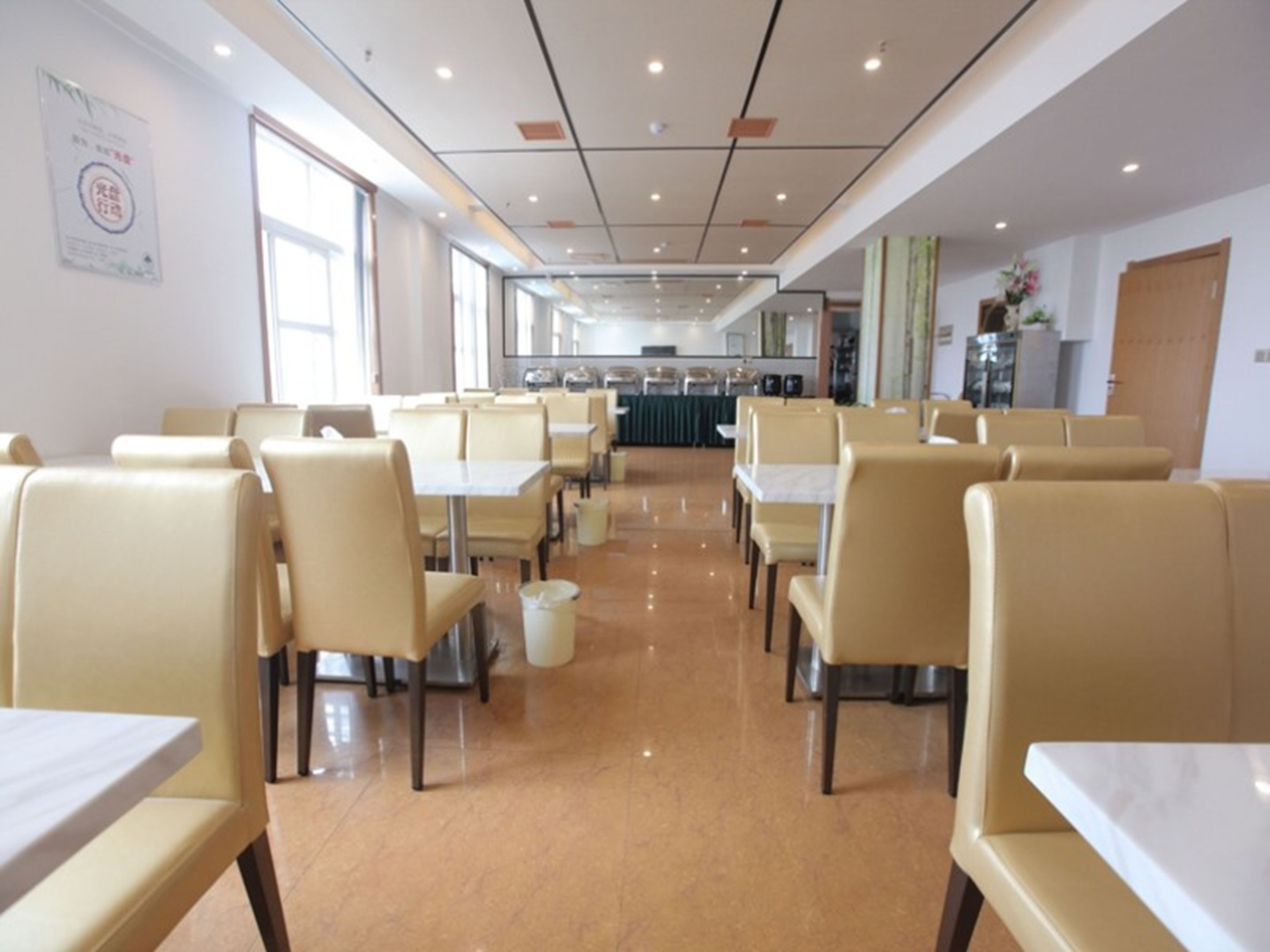 A spacious cafeteria with high tables and chairs, a tiled floor, and a large window providing natural light.