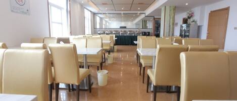 A spacious cafeteria with high tables and chairs, a tiled floor, and a large window providing natural light.