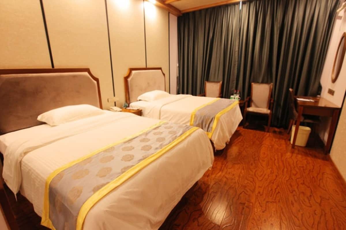 Ein Hotelzimmer mit zwei Betten, Holzboden, einem Schreibtisch und einem Stuhl.