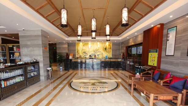 Un vestíbulo de hotel con una mesa de recepción, un gran emblema circular en el suelo, una zona de estar con muebles de madera y una pared con un mapa y carteles informativos.
