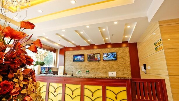 A reception area with a wooden reception desk, a large vase of flowers, and a wall-mounted TV.