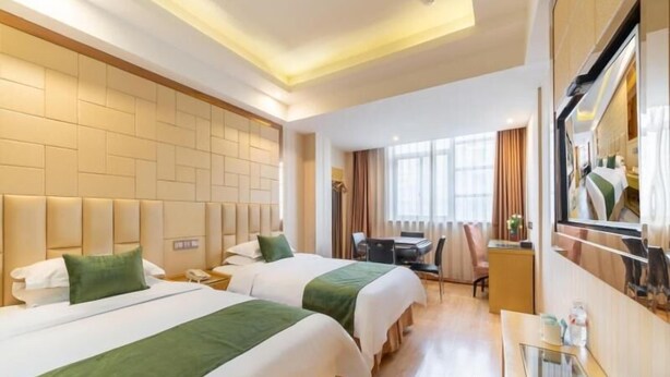 A hotel room with two beds, a desk, a chair, a TV, and a window with curtains.