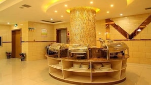 A hotel lobby with a central round buffet table, a large decorative pillar, and a mirrored wall.