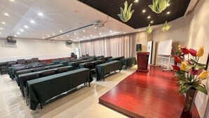 Uma sala de conferência com fileiras de mesas, um palco com um púlpito e um projetor.