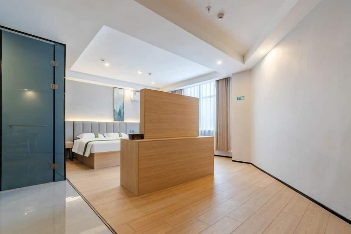 A hotel reception area with a wooden reception desk, a bed with a headboard, and a large window with curtains.