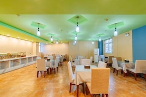 Un espace repas comprenant plusieurs tables et chaises, un comptoir avec un présentoir et une fenêtre laissant entrer la lumière naturelle.