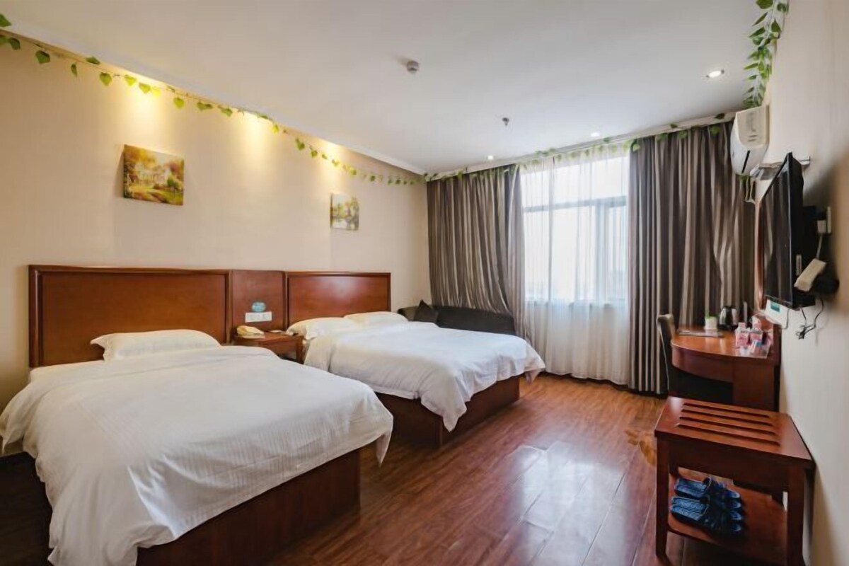 A hotel room with two beds, wooden flooring, a desk with a chair, and a television on the wall.
