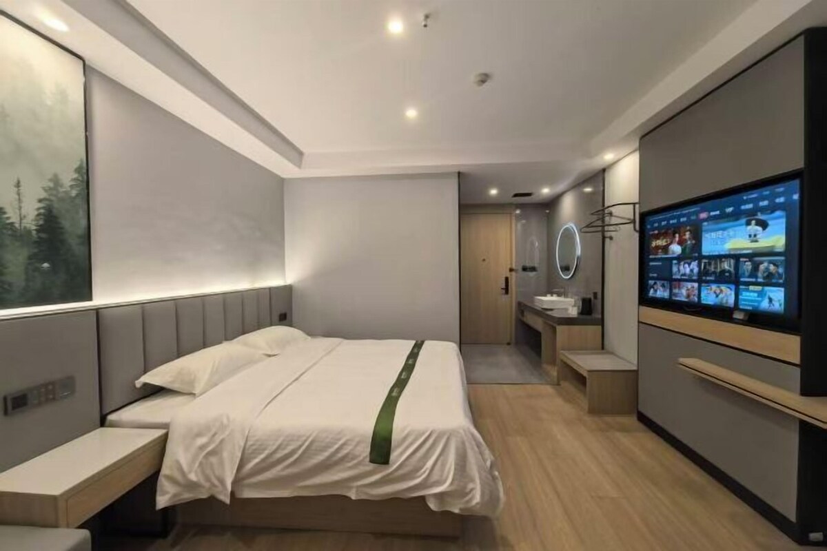 A modern hotel room with a bed, bedside table, TV, and a view of a forest through the window.